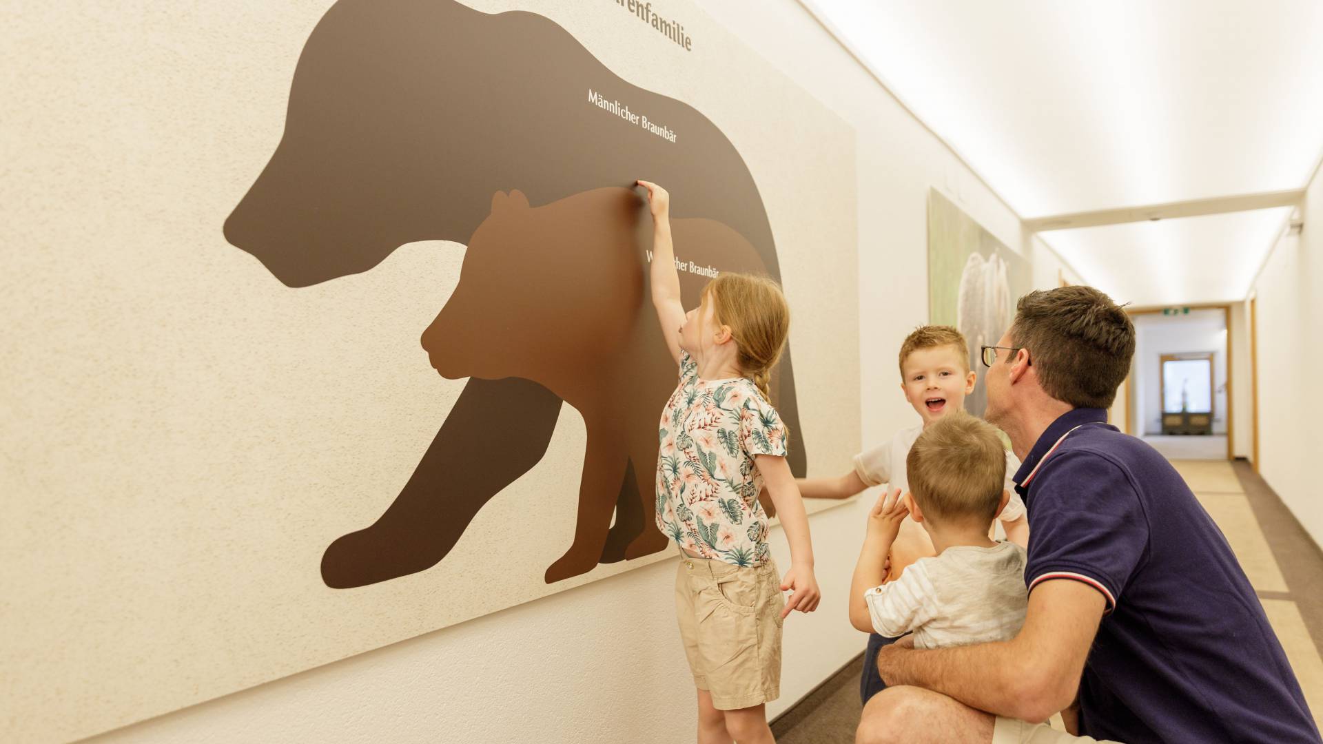 Vater mit Kindern vor großem Wandbild mit Bären