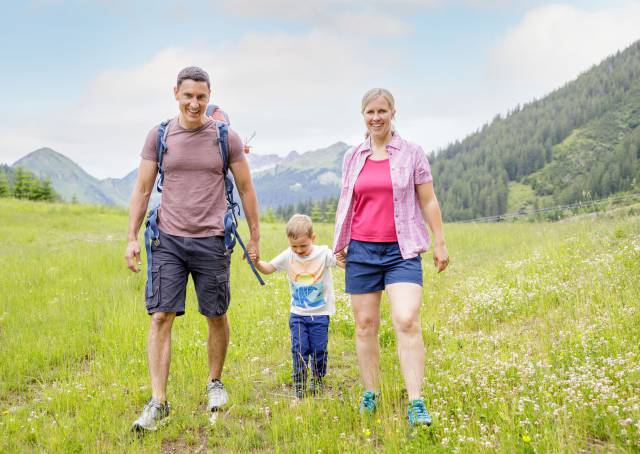 Eltern mit Sohn wandern über Wiese in Berwang