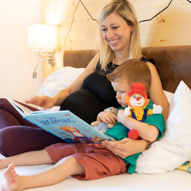 Mutter liegt mit Sohn im Bett und ließt ein Buch