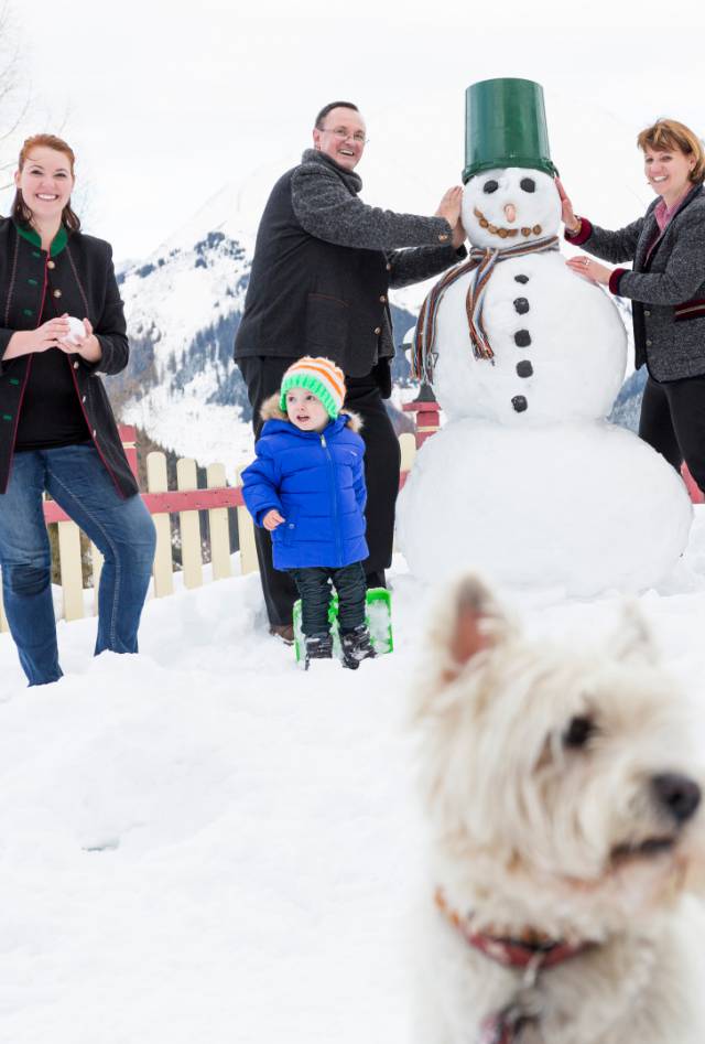 Die Gastgeberfamilie mit Hund und Bärtram bauen einen Schneemann