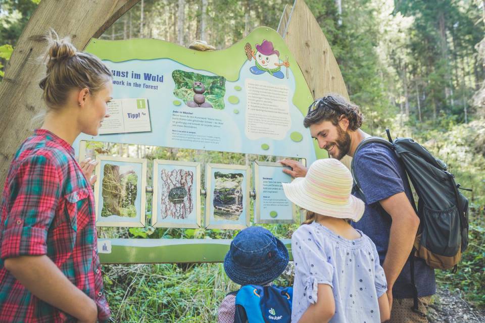 A family stands together in front of the information board for the Ehrwald Water Adventure Trail.