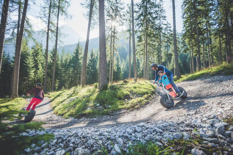 Familie fährt mit Monsterrollern in einem Wald in Tirol bergab 