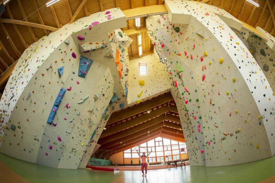A woman stands inside the Ehrwald Climbing Hall, between two freestanding climbing pillars.