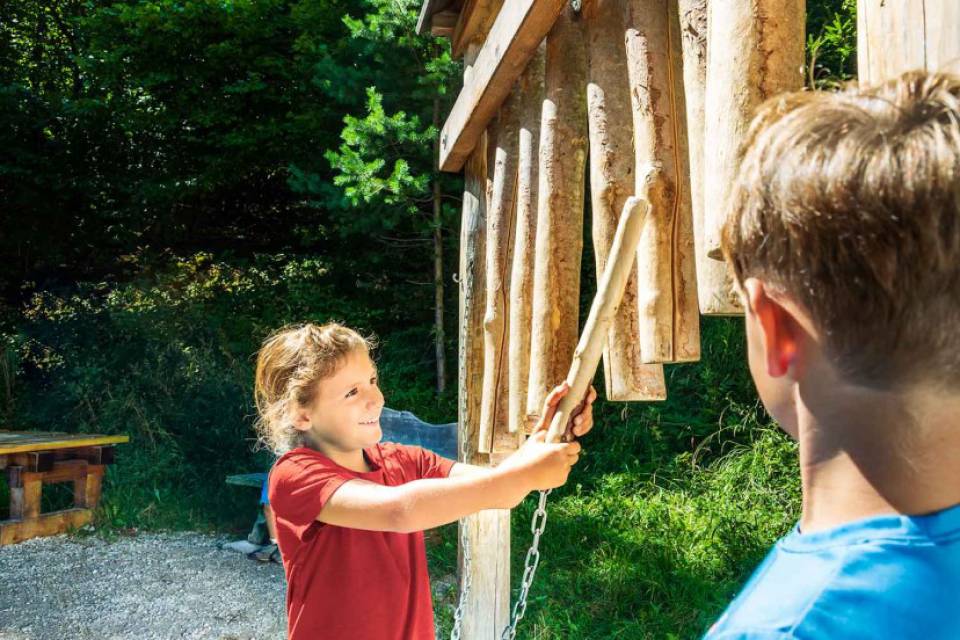 Mädchen spielt mit Holzklangstäben im Freien, Junge schaut zu