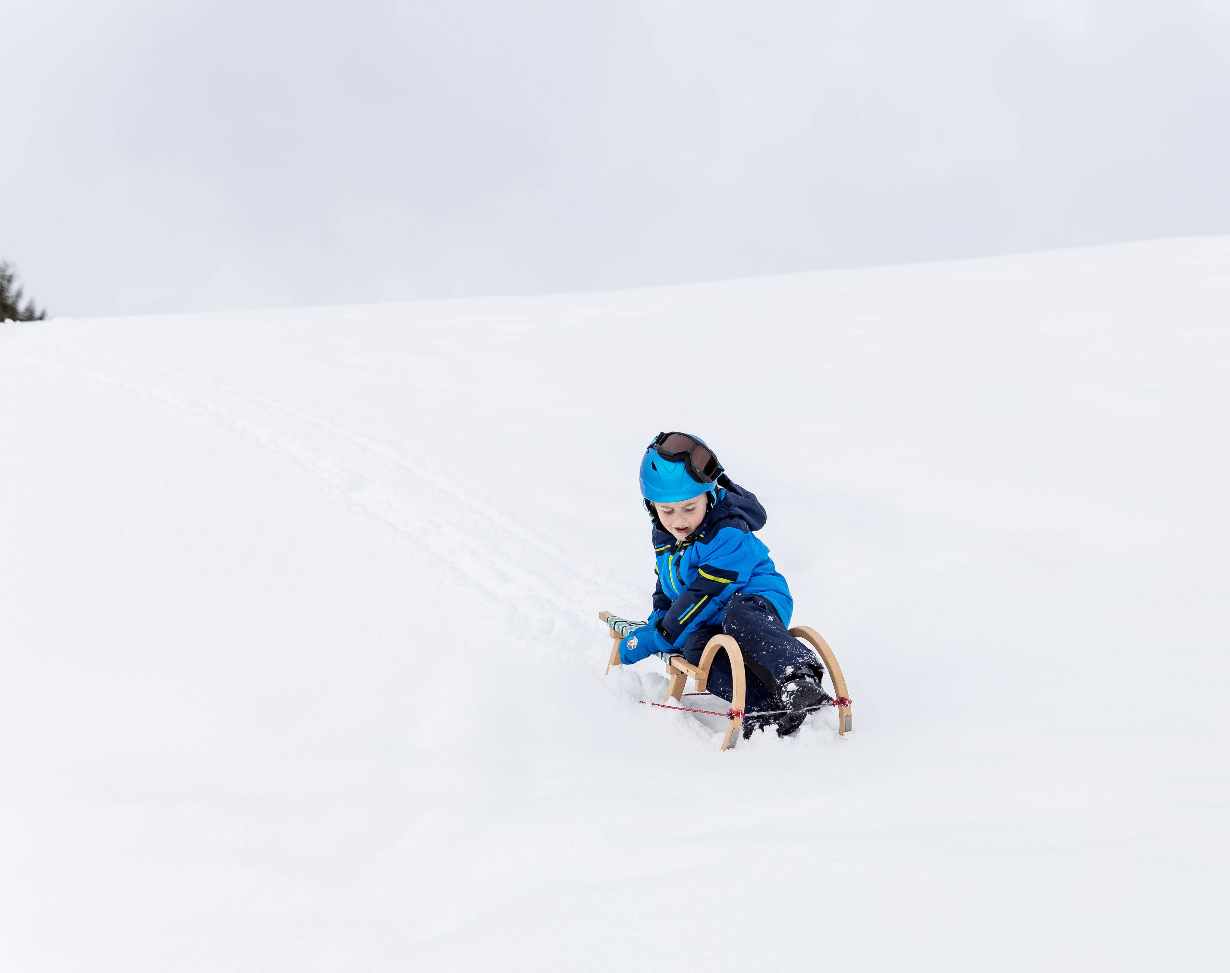 Kind fährt auf Schlitten den Schneeberg hinunter in Tirol