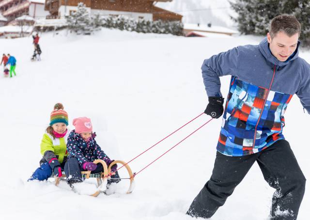 Vater mit Kindern auf Schlitten mit seinen Kindern im Schnee