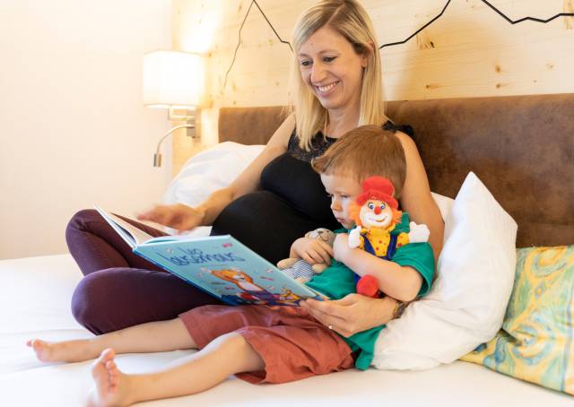 Mutter liegt mit Sohn im Bett und ließt ein Buch