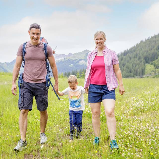 Eltern mit Sohn wandern über Wiese in Berwang