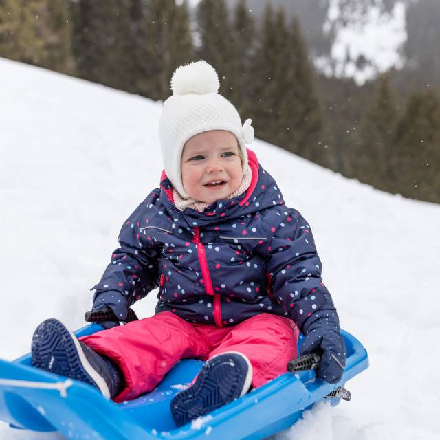 Kind sitzt im Schnee auf einem Schlitten in Tirol