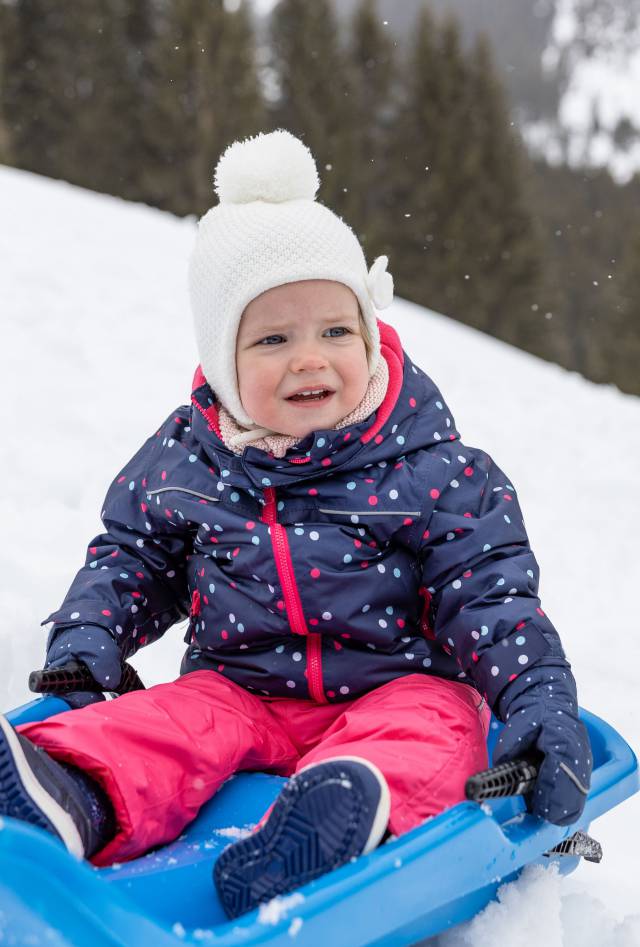 Kind sitzt im Schnee auf einem Schlitten in Tirol