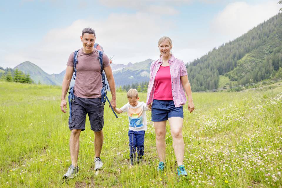 Eltern mit Sohn wandern über Wiese in Berwang