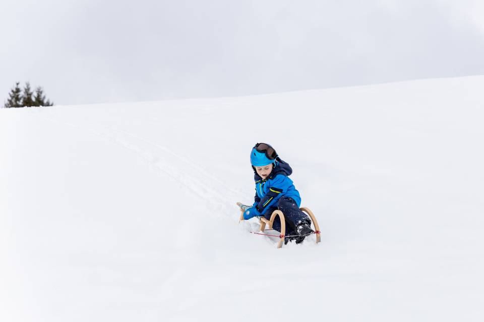 Kind fährt auf Schlitten den Schneeberg hinunter in Tirol