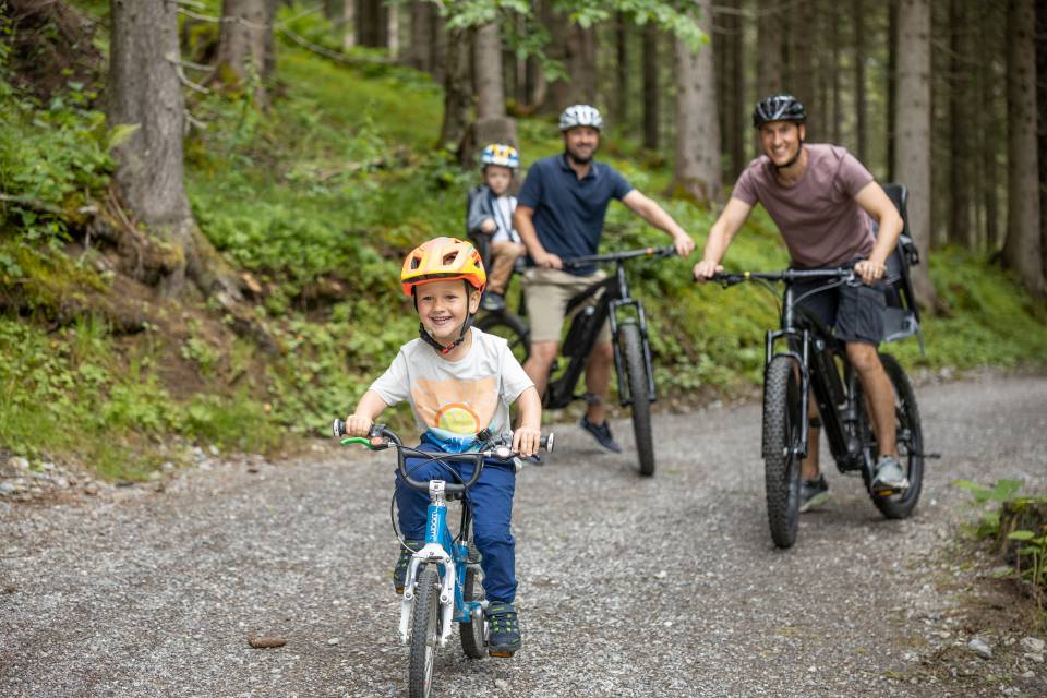 Väter mit Kindern beim Mountainbike fahren durch den Wald in Berwang