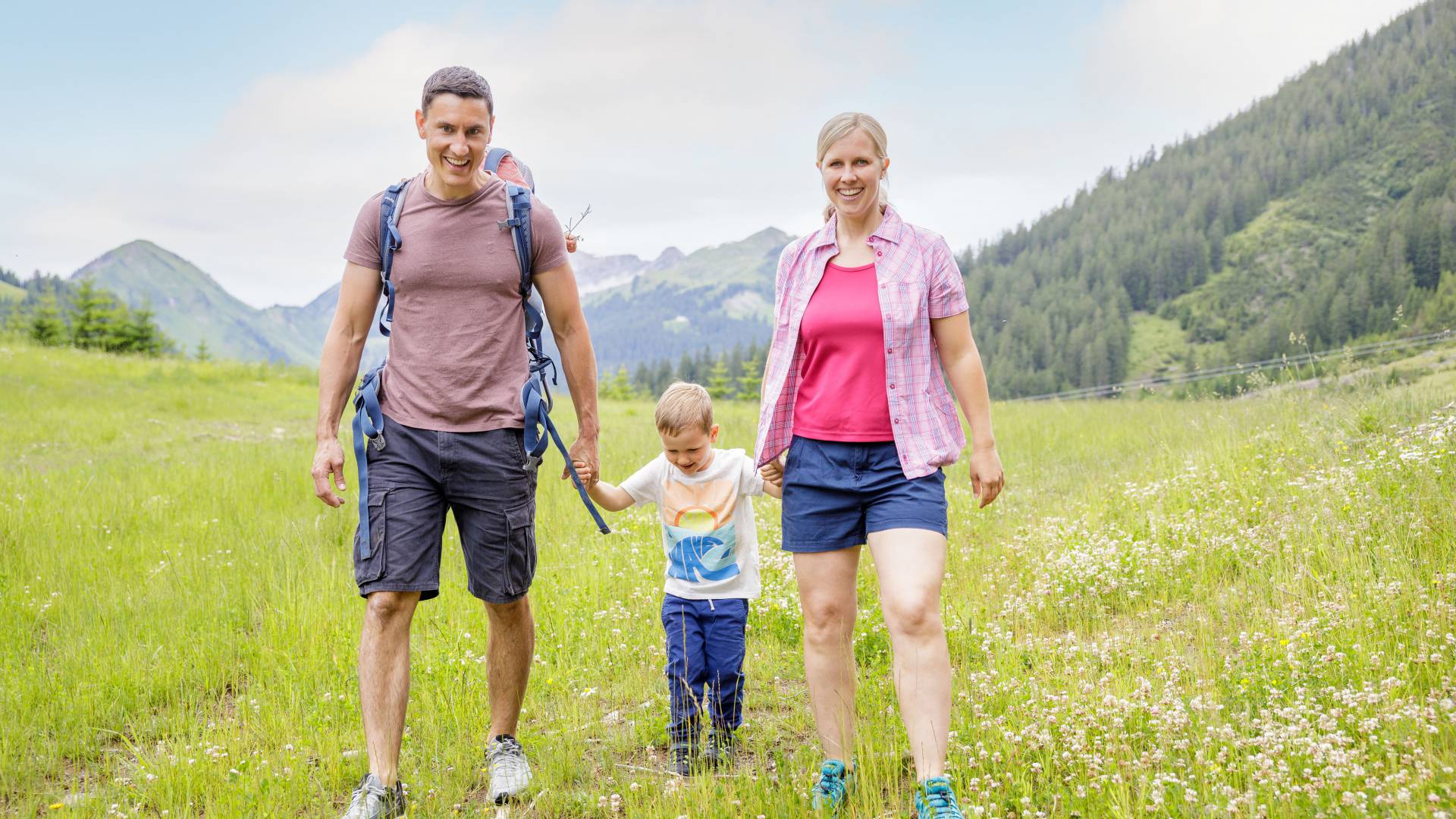 Eltern mit Sohn wandern über Wiese in Berwang