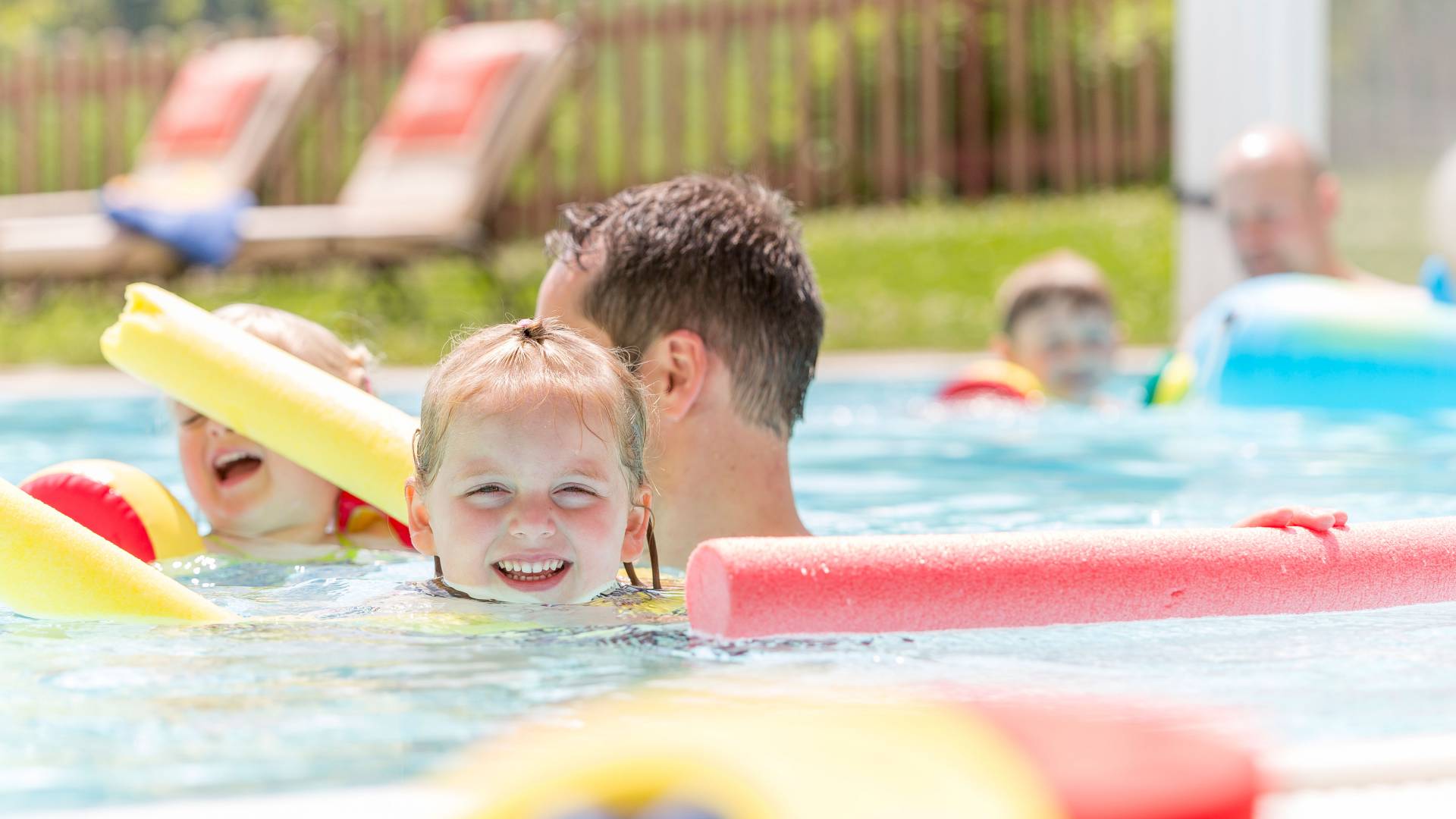 Kinder mit Eltern im Pool mit Schwimmnudeln