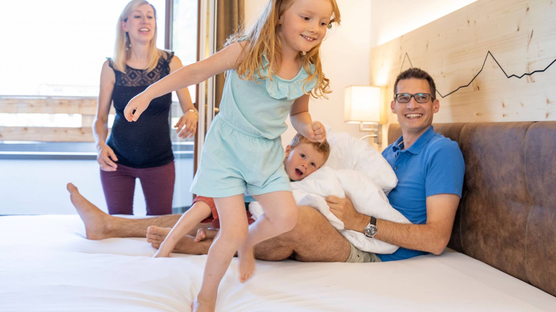 Kind rennt über Doppelbett, Familie sitzt dabei