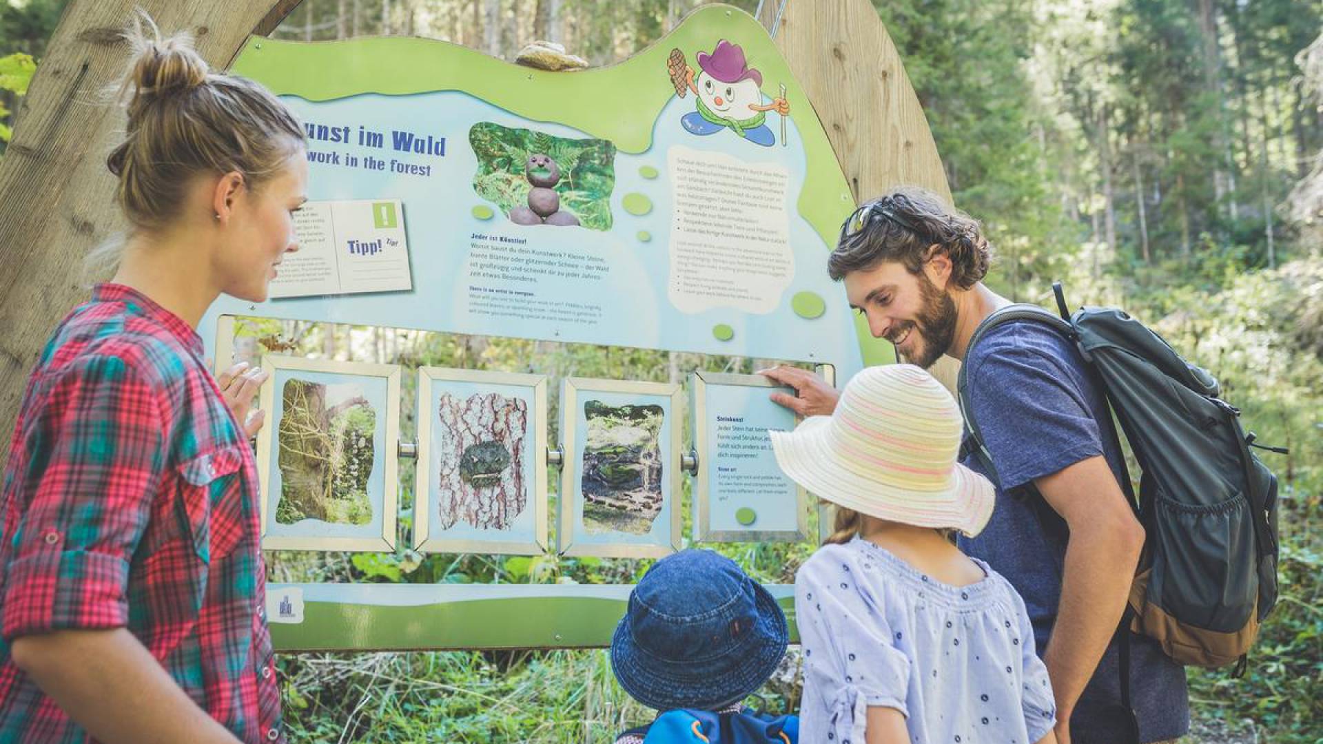Eine Familie steht gemeinsam vor einer Informationstafel vom Wassererlebnisweg Ehrwald.
