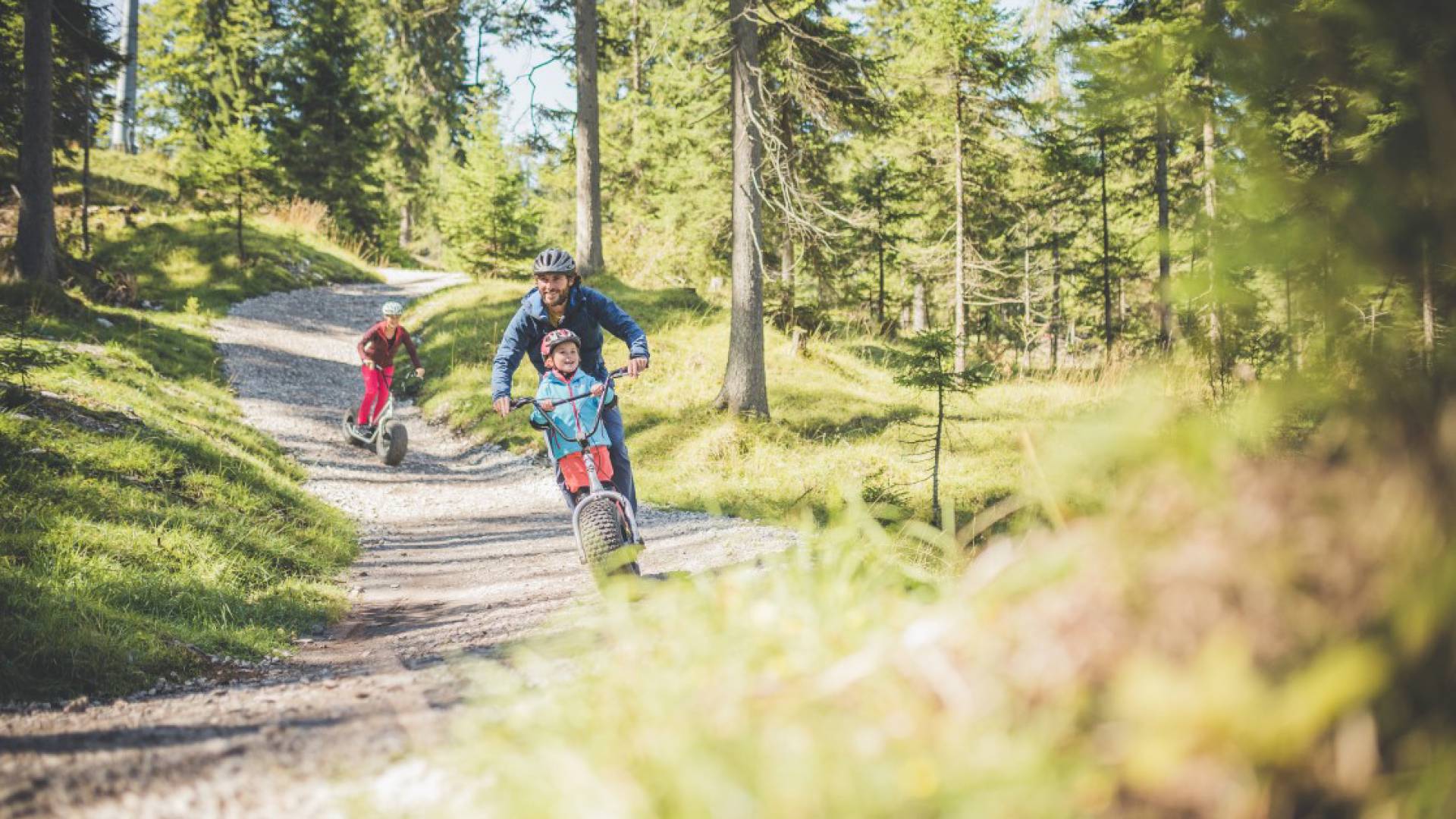 Familie fährt mit Rollern durch den Wald bei Berwang in der Nähe des Familienhotels Kaiserhof.